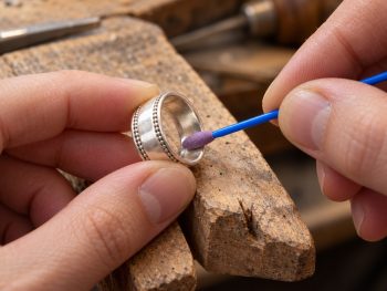 Small Micro-Mesh polishing swab finishing the inside of a silver ring on a jeweller’s bench pin.